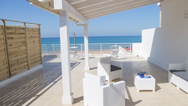 A covered outdoor area with white wicker furniture, a wooden fence, and a view of the sea. - Villa Sabbie D'oro (Cava D'aliga)
