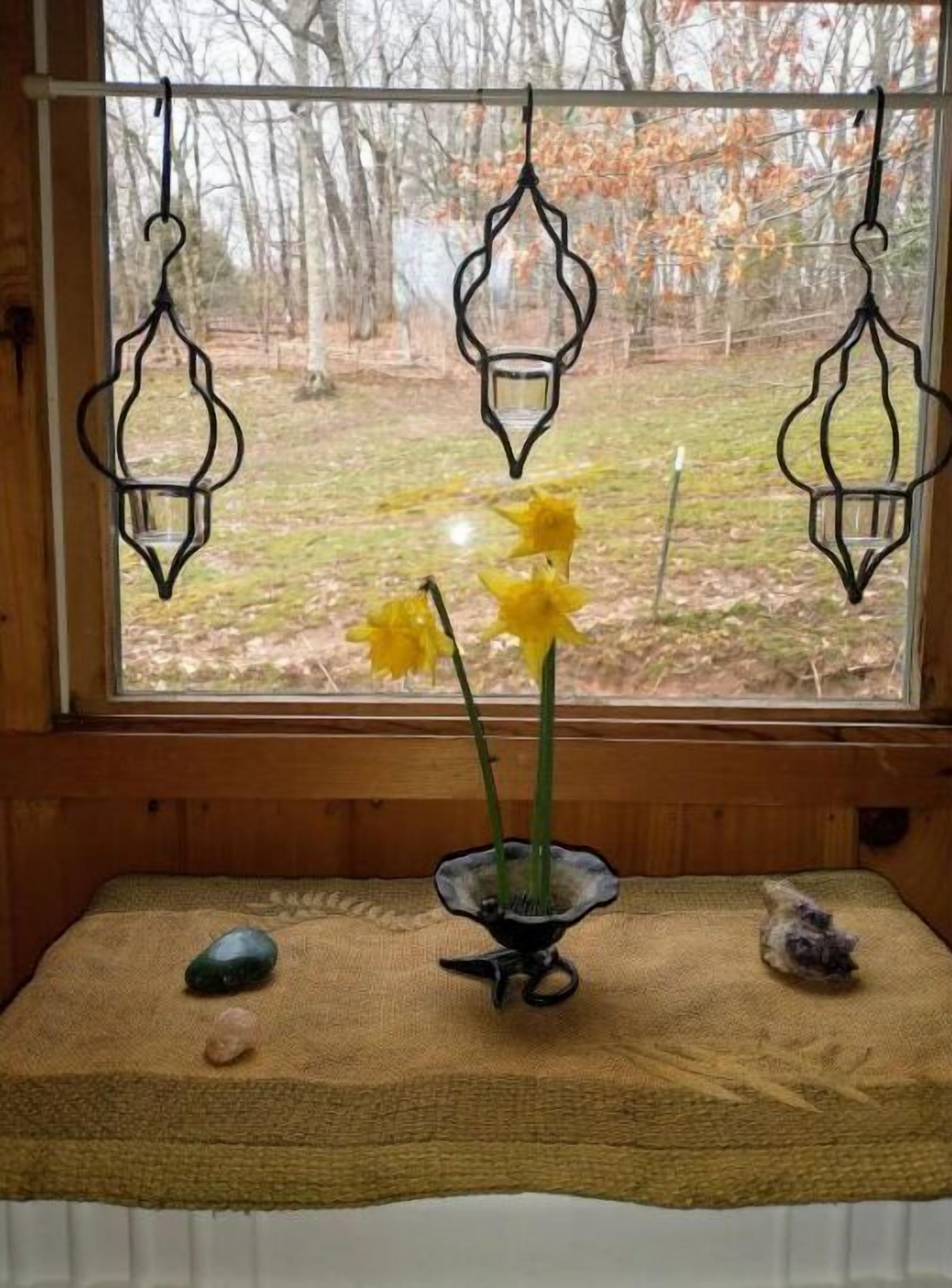 Una ventana con tres faroles colgantes y un jarrón con flores amarillas sobre un felpudo texturizado.