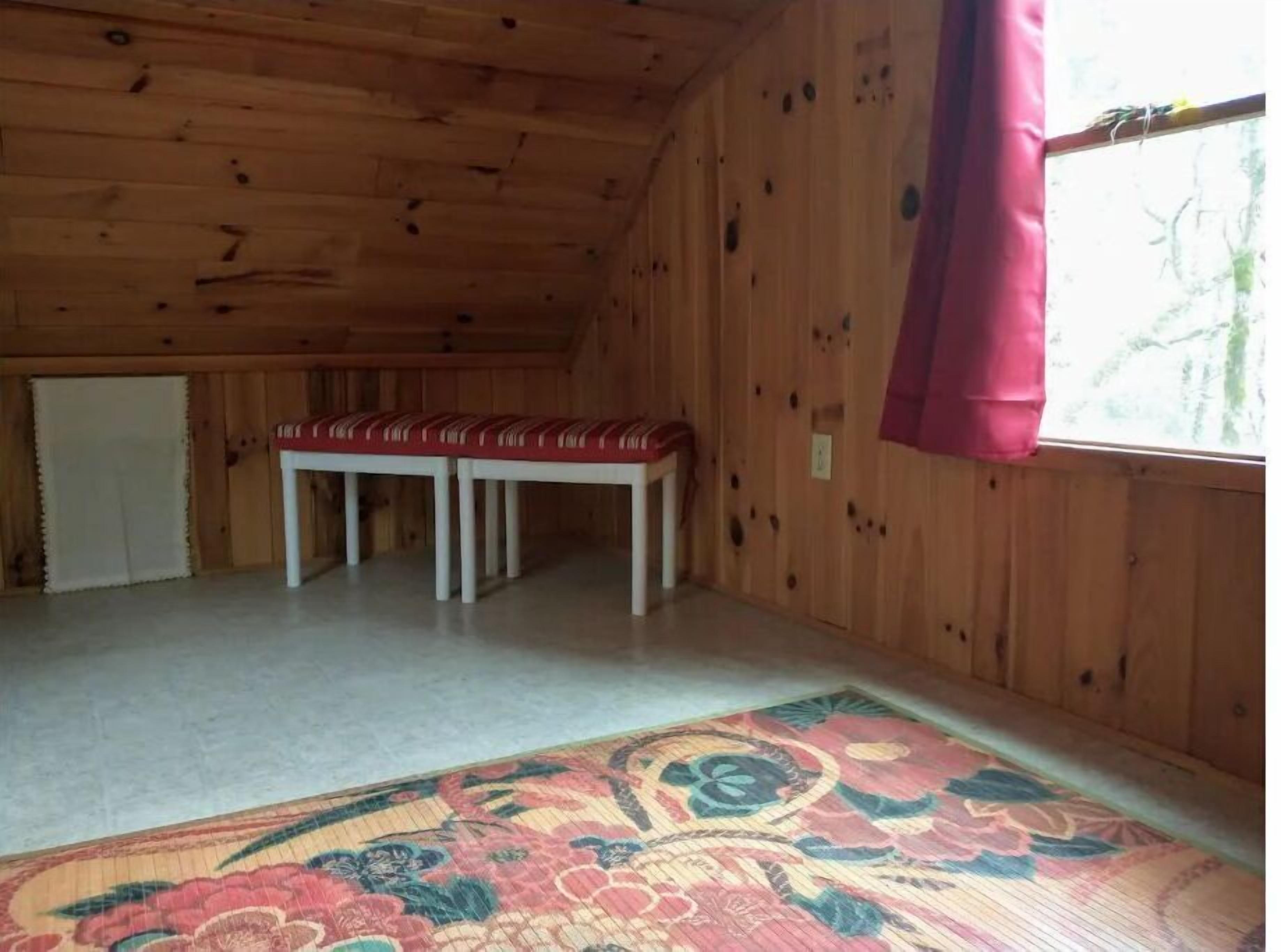 A wooden cabin interior with a bench, a rug, and a window with a curtain.