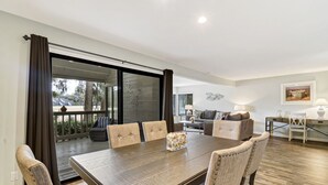 Een ruime eethoek met een grote tafel en zes stoelen, een glazen schuifdeur die leidt naar een terras, een zithoek en een schilderij aan de muur.