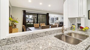 Een moderne keuken met granieten aanrechtbladen, roestvrijstalen spoelbakken en een eethoek met een tafel en stoelen.