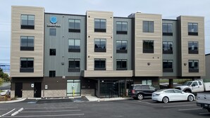 A modern hotel with a flat facade, multiple windows, and a parking lot with cars.