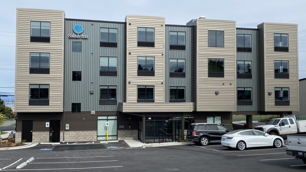 A modern hotel with a flat facade, multiple windows, and a parking lot with cars.