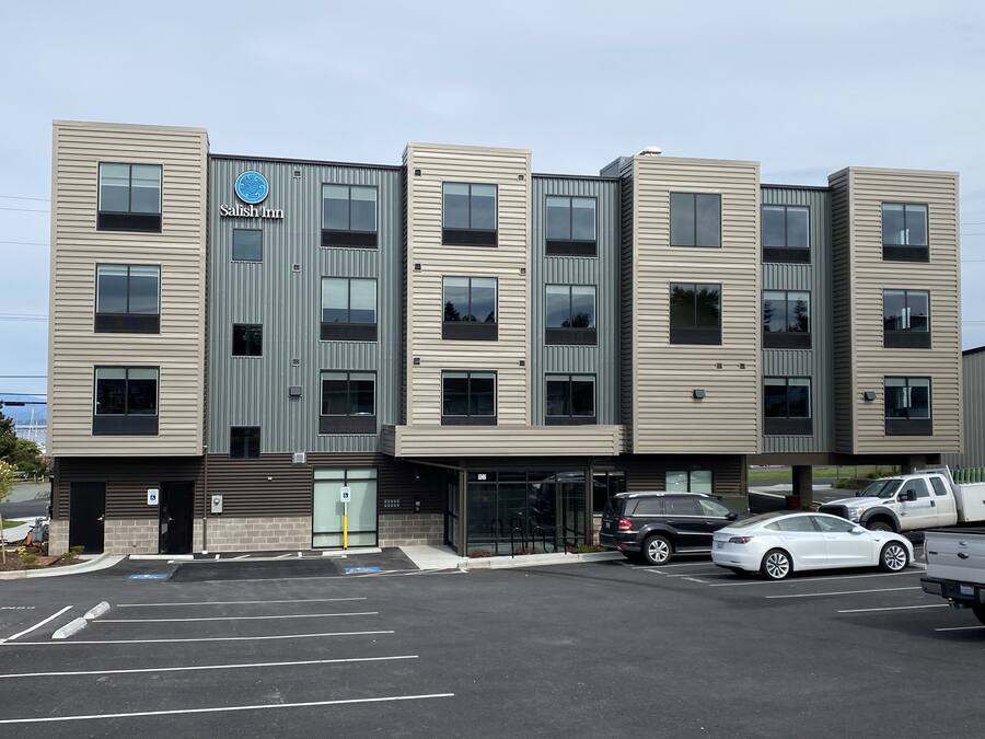 A modern hotel with a flat facade, multiple windows, and a parking lot with cars.