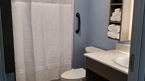 A bathroom with a shower curtain, toilet, sink, and towel storage.
