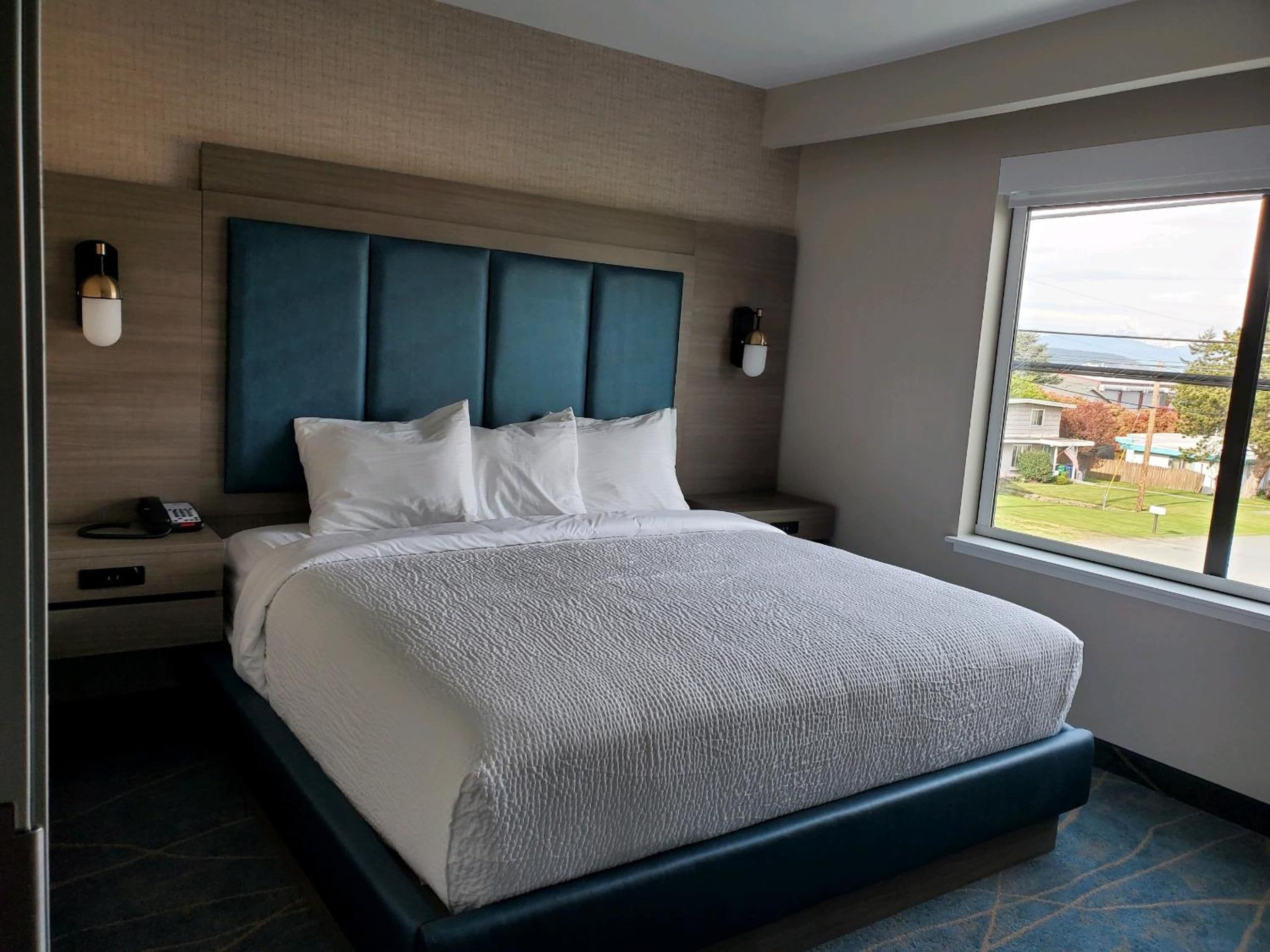 Una camera d'albergo con un letto grande, una testiera, comodini, un telefono e una finestra vista.