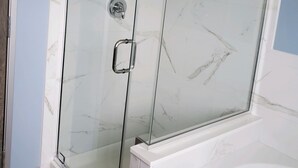 A glass-enclosed shower with a marble backsplash and a bathtub.