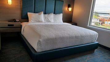 A hotel room with a large bed, a headboard, bedside lamps, a nightstand with a phone, and a window with a view of the outside.