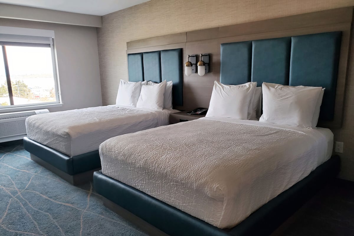 A hotel room with two beds, a large window, and a wall-mounted light fixture.