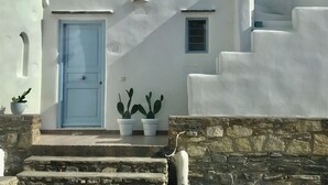 Un bâtiment blanc avec une porte bleue, deux plantes en pot et un mur de pierre.