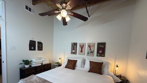 Un dormitorio con una cama grande, ventilador de techo y obras de arte en la pared.
