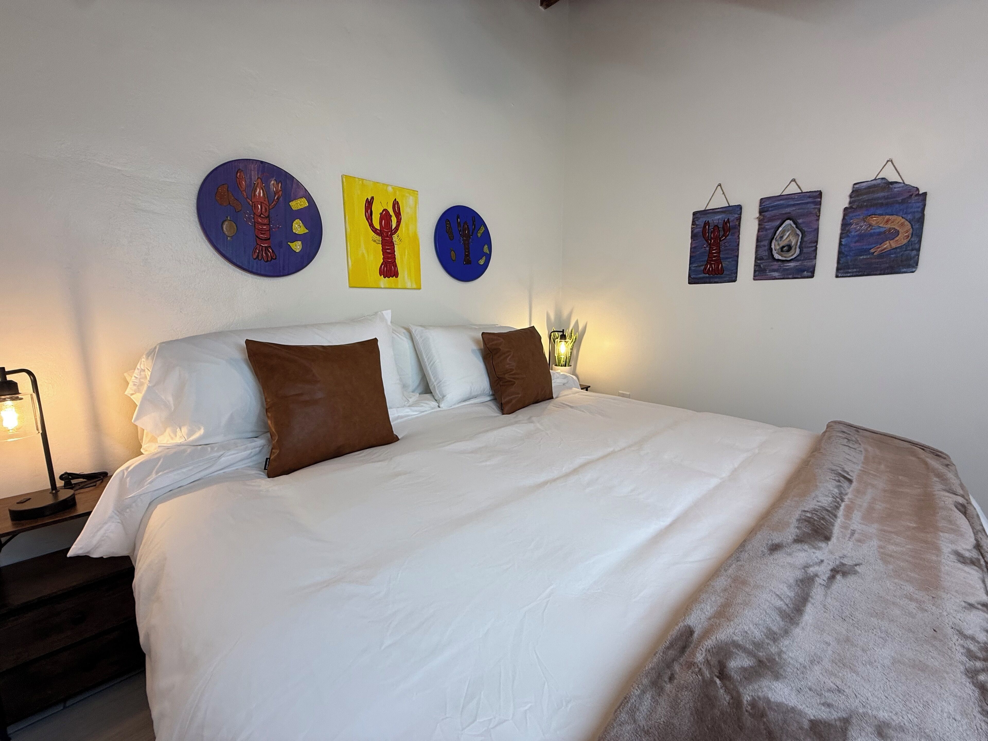 A neatly made bed with white linens and brown pillows, a bedside lamp, and wall art depicting various sea creatures.