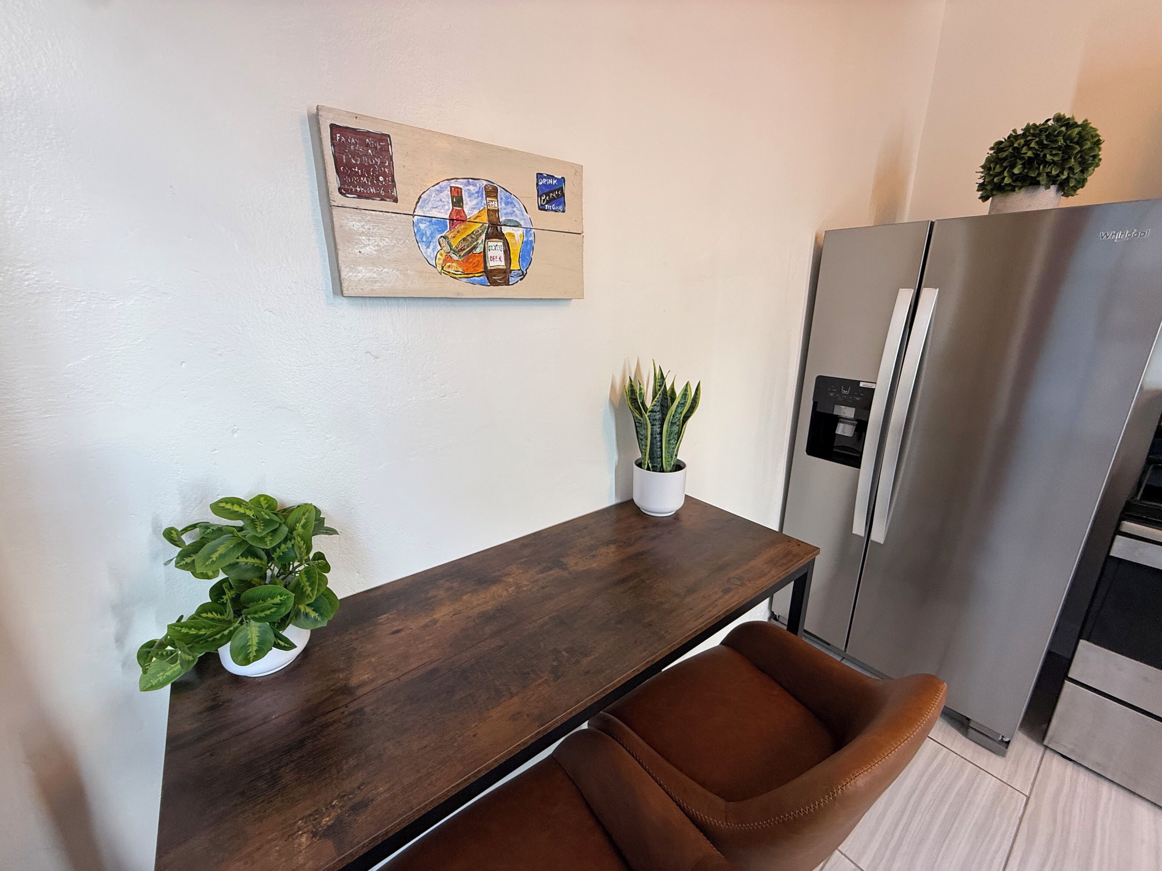A kitchen with a wooden table, a refrigerator, and two potted plants.