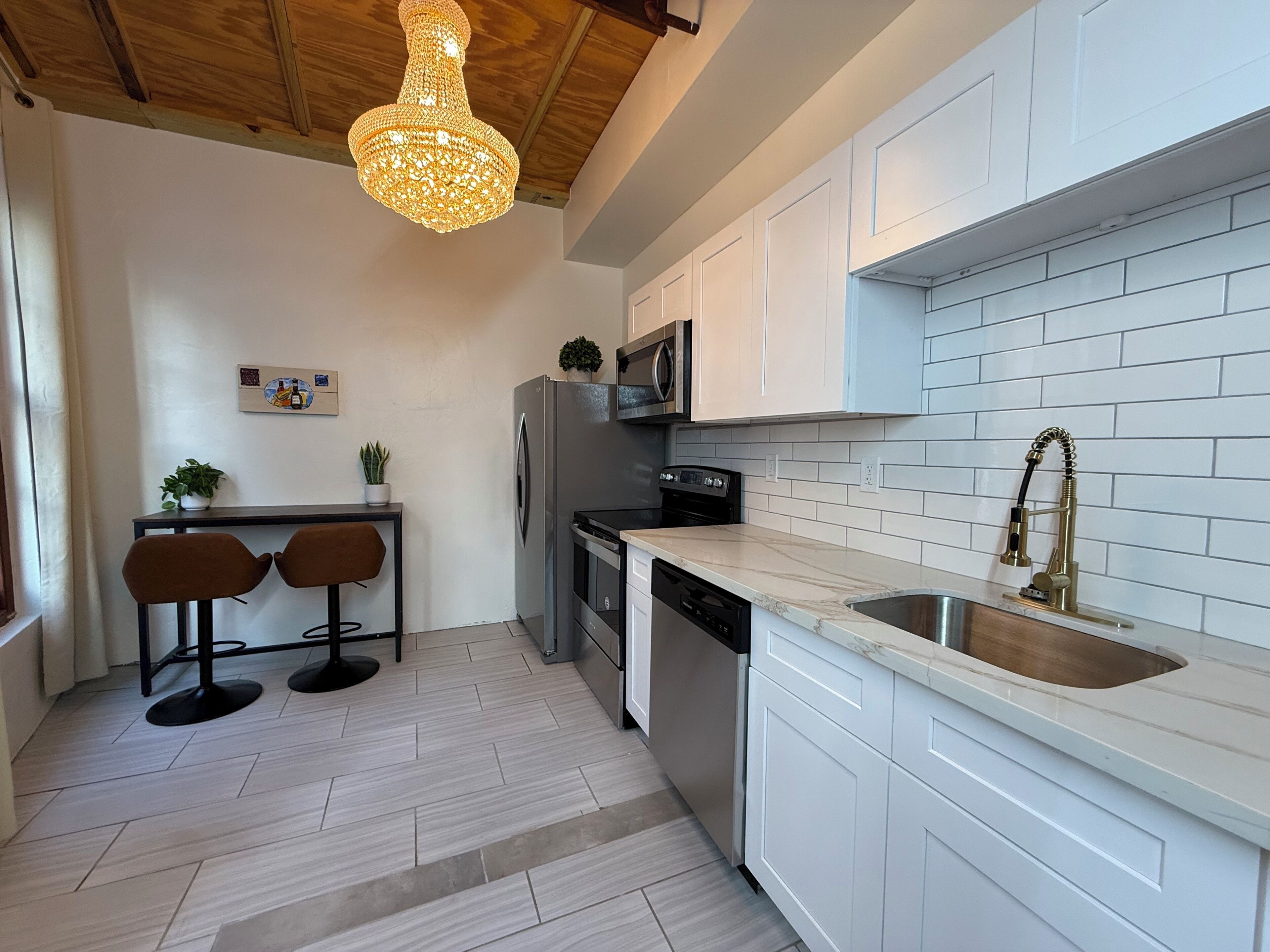 Eine moderne Küche mit weißen Schränken, einer Spüle aus Edelstahl, einer Mikrowelle und einem Geschirrspüler. Die Decke ist aus Holz und es gibt eine Hängeleuchte.