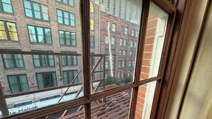 Vista a través de una ventana con marco de madera, que da a un edificio de ladrillo con múltiples ventanales y una escalera metálica.