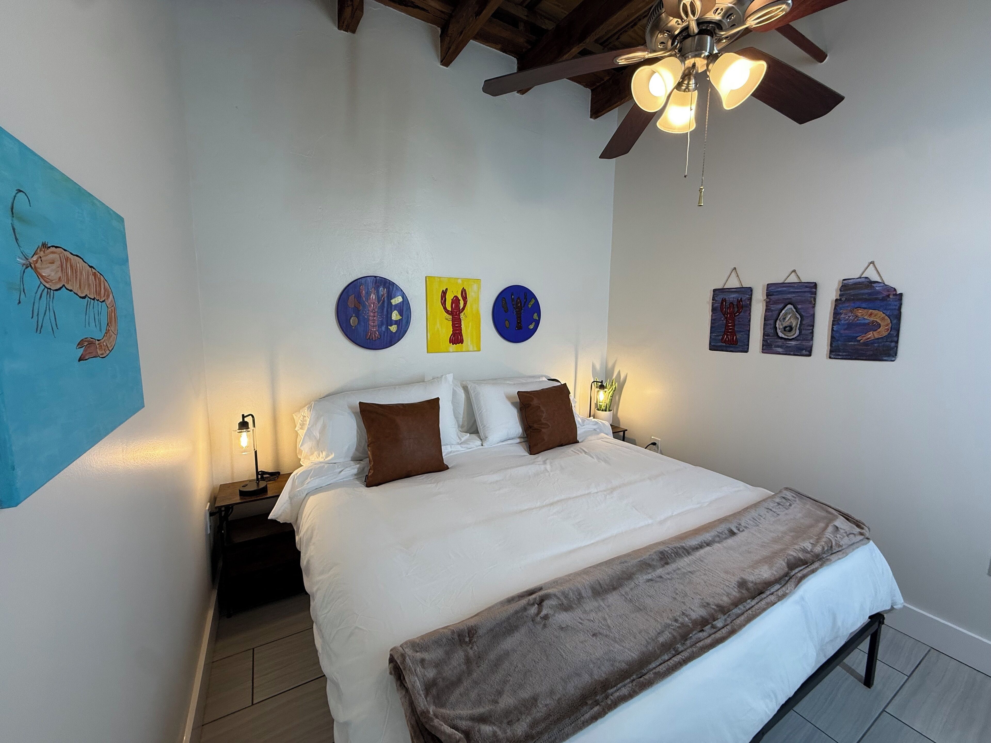 A bedroom with a bed, a ceiling fan, and wall art.