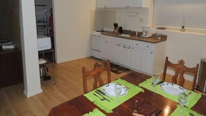 Une cuisine compacte avec des meubles blancs, une table à manger en bois pour deux personnes et un ventilateur de plafond.