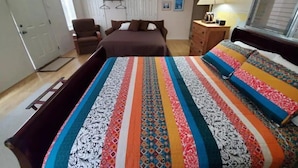Une chambre à coucher avec un grand lit, une chaise, une commode, un ventilateur de plafond et une fenêtre.