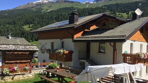 A chalet with a wooden exterior, a balcony with flower boxes, and a picnic table in the yard. - THREE-ROOM APARTAMENT  2 BATHROOM
BIKE TREKKING  MOUNTAIN VALFURVA STELVIO GAVIA (Santa Caterina)