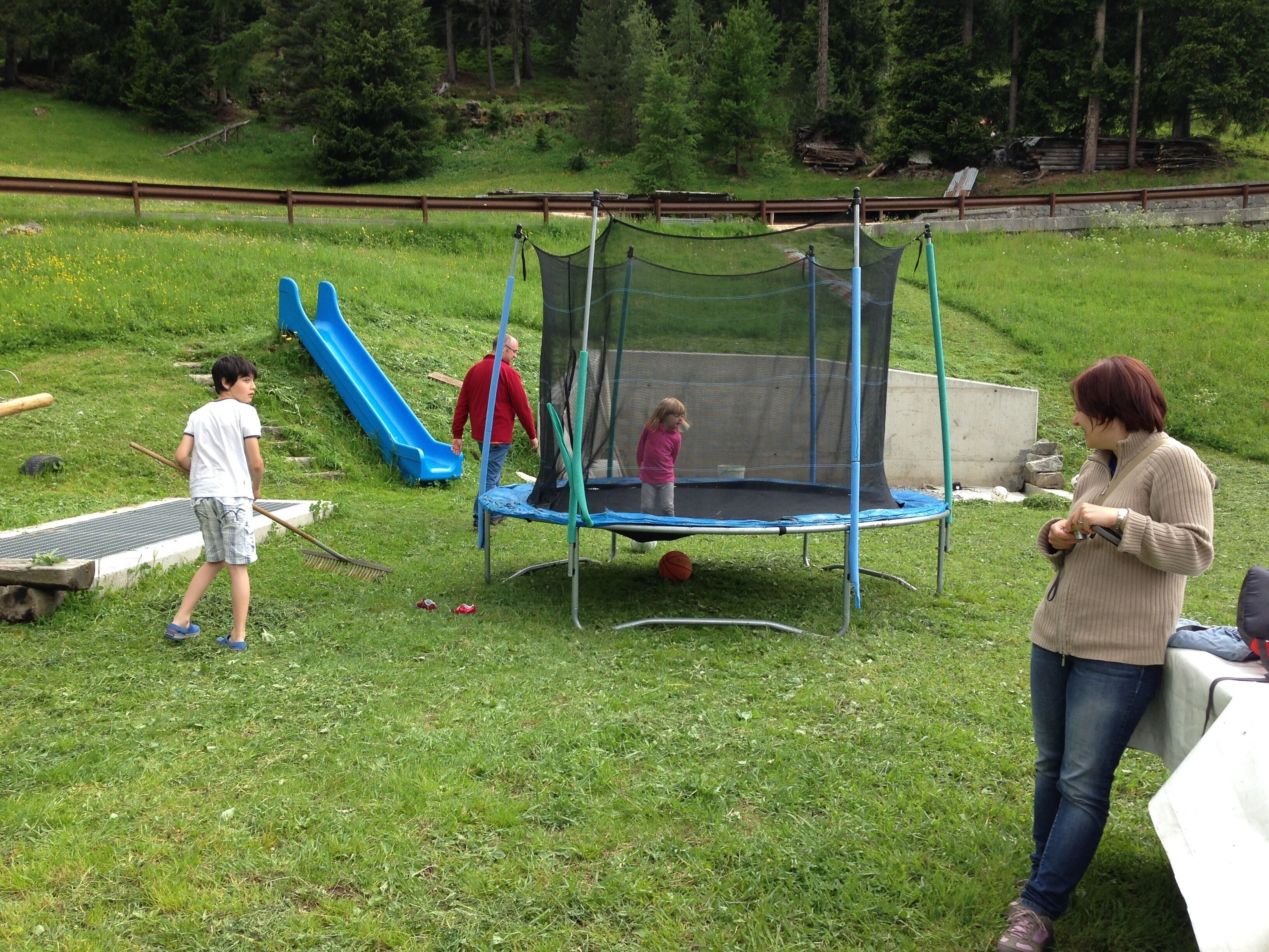 Un trampoline installé dans un espace herbeux, avec un toboggan à proximité.