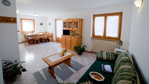 A spacious living area with a dining table, wooden cabinets, a sofa, and a large window. - THREE-ROOM APARTAMENT  2 BATHROOM
BIKE TREKKING  MOUNTAIN VALFURVA STELVIO GAVIA (Santa Caterina)