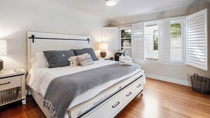 A bedroom with a bed, bedside tables, a lamp, a nightstand, a window with shutters, and a ceiling light. - Spanish Home: Steps to Beach & 2nd St
-Quiet part of Belmont Shores (Long Beach)