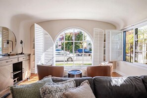 Un salón acogedor con un amplio ventanal arqueado, sofás de cuero, una mesa de centro y un mueble de madera con espejo.