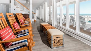 Un balcon spacieux avec des chaises et un banc en bois, un escalier et de grandes fenêtres offrant une vue sur l’océan.