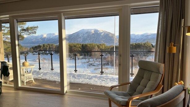 Habitación con amplios ventanales que ofrecen vistas a un paisaje nevado y montañas.