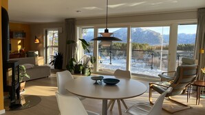 Una sala de estar moderna con comedor, ventanas amplias con vista a la montaña y una zona de estar acogedora.