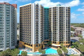 Um hotel alto com várias varandas, uma piscina e área ajardinada à beira da piscina.