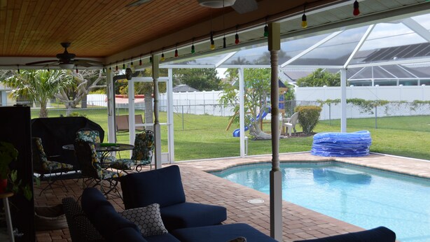 Un espace extérieur abrité comprenant une piscine, des sièges et une vue sur un jardin.