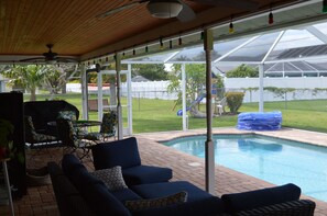 A covered outdoor area with a pool, seating, and a view of a backyard. - Spacious, remodeled, perfect for two family gatherings, (Cape Coral)
