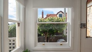 Ein Zimmer mit einem Holztisch, einem kleinen Topfpflanzen und Blick auf einen Baum und ein Gebäude durch ein Fenster.