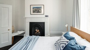 Ein Schlafzimmer mit einem Bett, einem Kamin, einem gerahmten Bild an der Wand und einem Fenster mit Vorhängen.