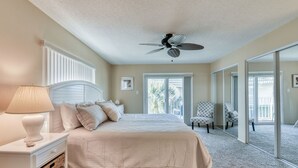 A bedroom with a bed, nightstand, lamp, and a ceiling fan. - Direct Ocean from Balcony (Indialantic)