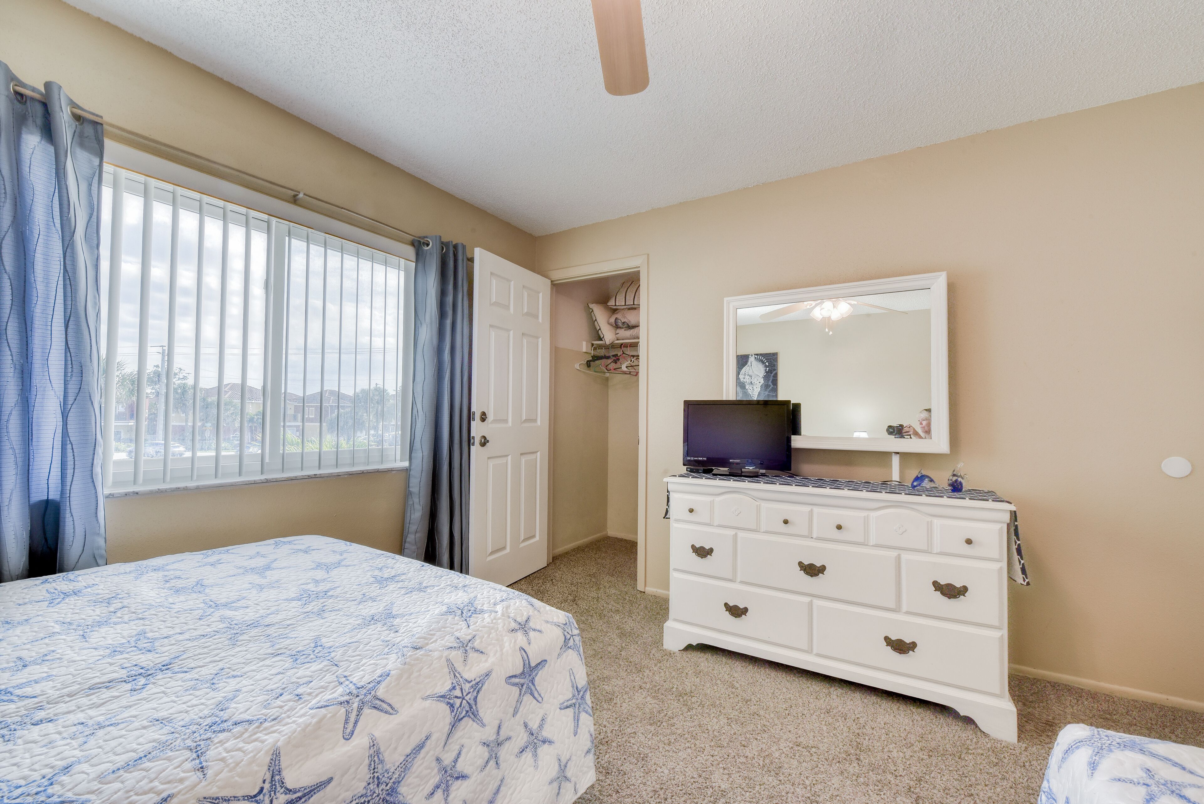 A bedroom with a bed, dresser, and a window with curtains.