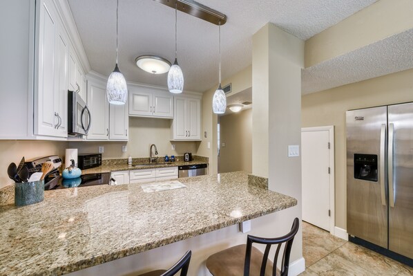 A kitchen with granite countertops, white cabinets, stainless steel appliances, and pendant lighting. - Direct Ocean from Balcony (Indialantic)