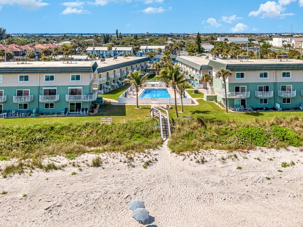 A beachfront hotel with multiple-story buildings, a swimming pool, and a sandy beach path leading to the pool. - Direct Ocean from Balcony (Indialantic)