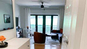 Ein modernes Wohnzimmer mit Holzboden, einem weißen Schrank, einem braunen Sessel und einem Essbereich mit Tisch und Stühlen.