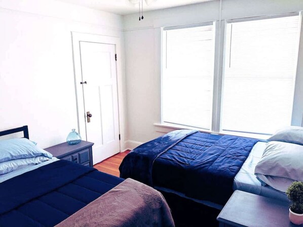 A bedroom with two beds, a small table, a door, and large windows. - Great Deal, Just A Few Blocks To Dwntn Hot Springs (Hot Springs)