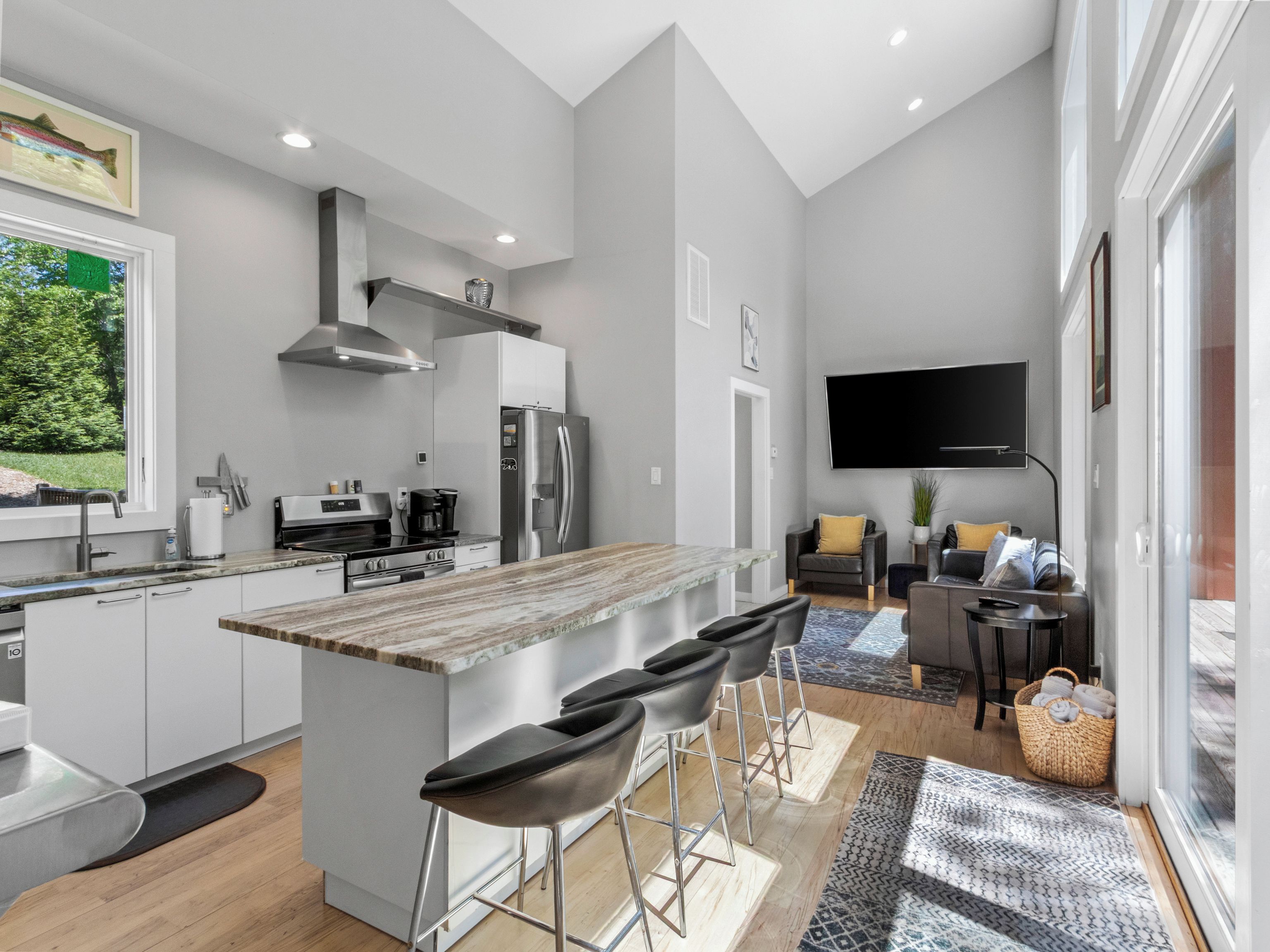 Una cocina moderna con una isla central, taburetes de bar, un televisor de pantalla plana y una zona de comedor con sofá y mesa de centro.