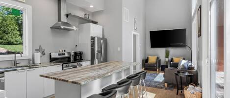 Una cocina moderna con una isla central, taburetes de bar, un televisor de pantalla plana y una zona de comedor con sofá y mesa de centro.
