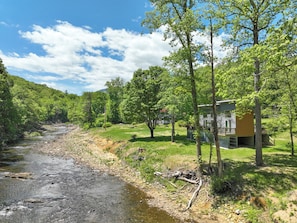 A riverside property with a cabin, surrounded by trees and a grassy area. - Hot Tub+Fire Pit, On the River, WiFi, Grill, Cozy! (Burnsville)