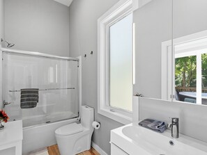 A modern bathroom with a glass-enclosed shower, a toilet, and a sink with a mirror above. - Hot Tub+Fire Pit, On the River, WiFi, Grill, Cozy! (Burnsville)