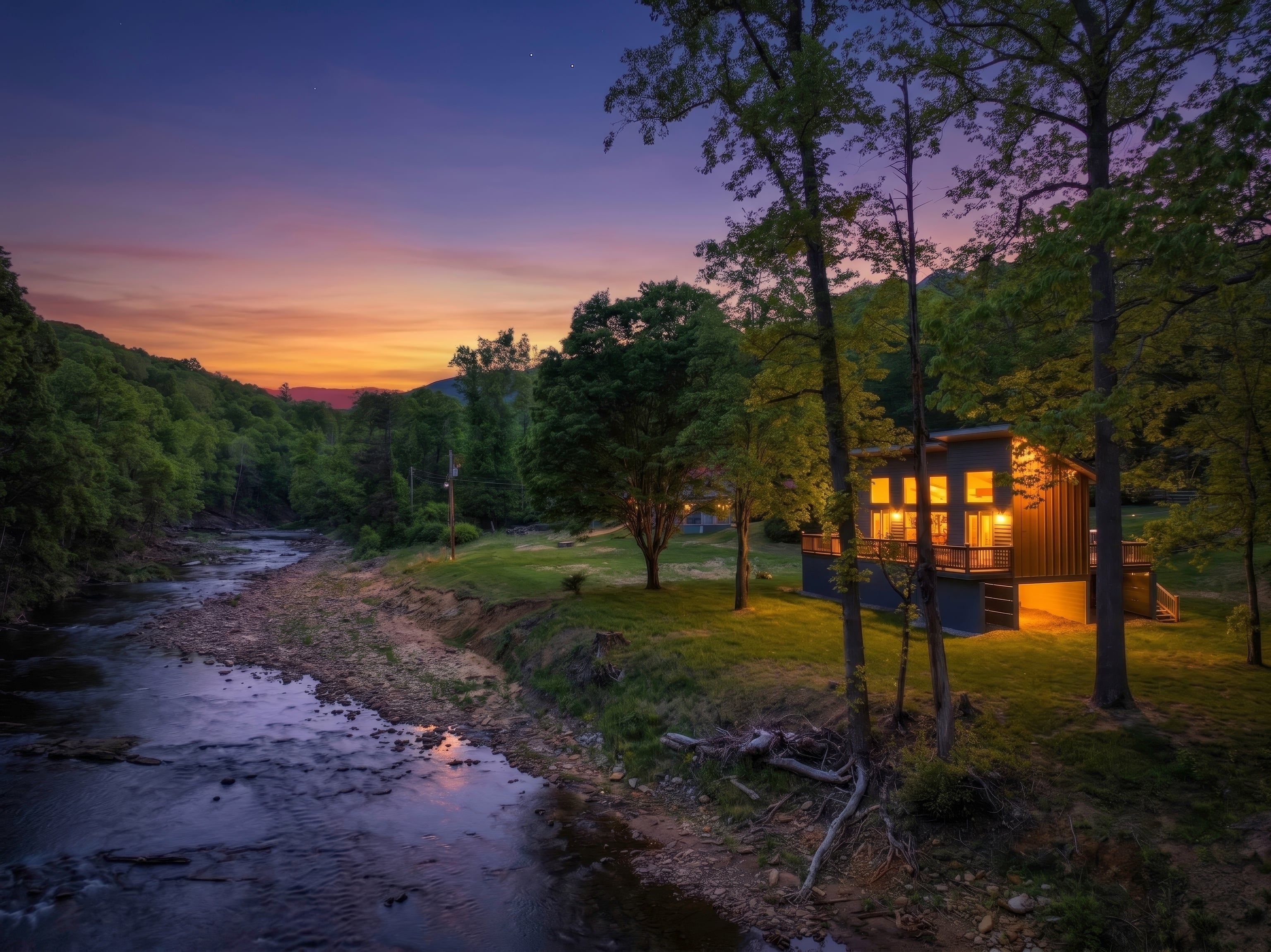 A cabin with a deck, surrounded by trees and a river.