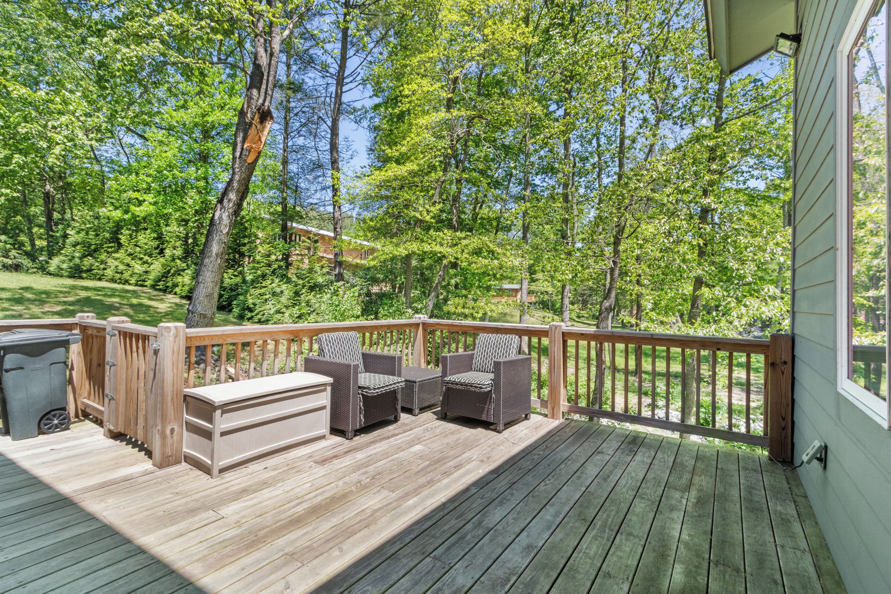 A wooden deck with outdoor furniture, a trash bin, and a view of a wooded area.