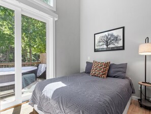 A bedroom with a large bed, a framed picture on the wall, and a view of a deck through a sliding glass door.