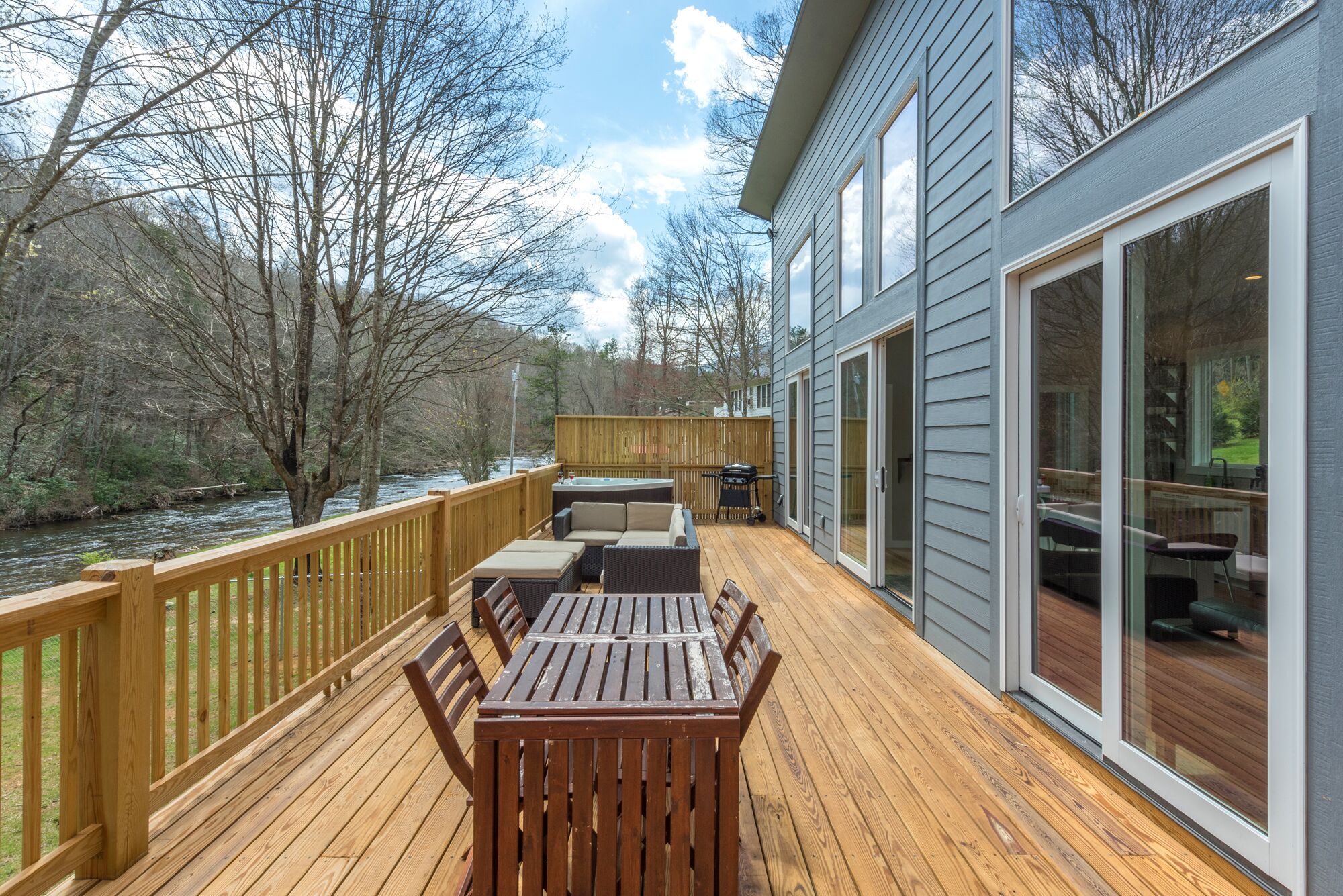 Une terrasse dotée de mobilier d’extérieur, offrant une vue sur une rivière, et un bâtiment avec de grandes fenêtres.