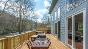 Eine Terrasse mit Gartenmöbeln, Blick auf einen Fluss und ein Gebäude mit großen Fenstern.
